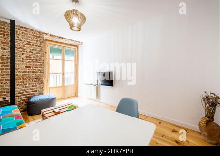 Soggiorno con tavolo da pranzo bianco, tv, pareti in mattoni bianchi e a vista e pavimenti in legno di pino Foto Stock