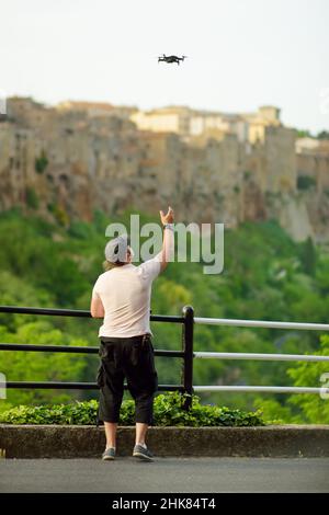 Un uomo che lancia un drone nei pressi della città di Pitigliano, situato in cima ad una cresta di tufo vulcanico. Scattare foto da quanto sopra. Fotografia digitale con droni. E Foto Stock
