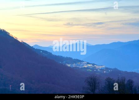 Le montagne del Caucaso al tramonto, un villaggio nelle luci notturne su un pendio di montagna. Rosa Khutor, Sochi, Russia, 2021 Foto Stock