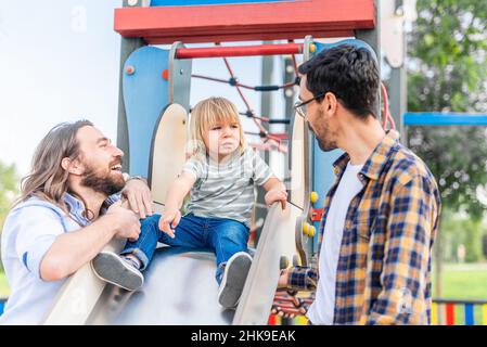 ragazzo sopra una diapositiva giocando con i suoi papà. Foto Stock