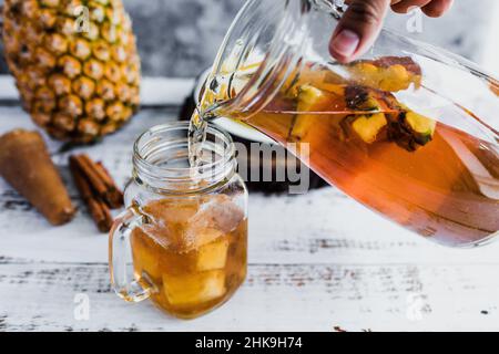 Tepache bevanda messicana di ananas fermentata e mano che tiene un vaso con kombucha superfood probiotico fatto in casa a fette di ananas bevanda in Messico Foto Stock