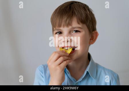 Primo piano ritratto allegro bambino divertirsi mangiando patatine isolate su sfondo grigio. Carino ragazzino che mangia patatine e sorride guardando la macchina fotografica. Il bambino caucasico mangia cibo spazzatura Foto Stock