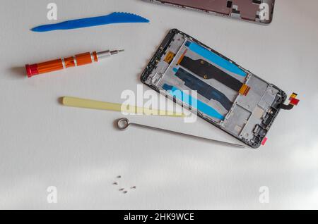 Repair of smartphones concept. Hand tool and disassembled phone lying on the table. Part of a series. Indoors. Selective focus. Foto Stock