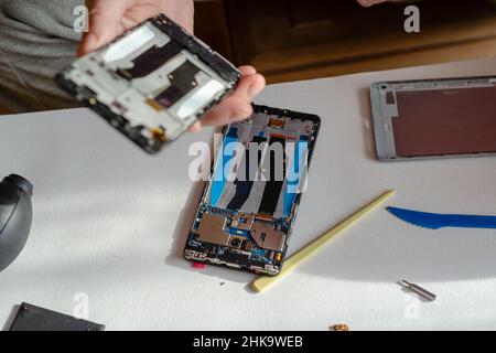 Repair of smartphones concept. A man holding a new display in his hand. A disassembled phone with an old, broken display lying on the table. Part of a Foto Stock
