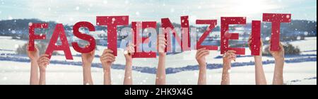 Persone mani tenere rosso tedesco parola Fastenzeit significa digiuno. Sfondo invernale nevoso con fiocchi di neve Foto Stock