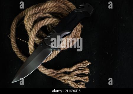 Coltello pieghevole tattico per la sopravvivenza, lo stile di vita attivo e la ricreazione, su sfondo di corda e sfondo scuro Foto Stock