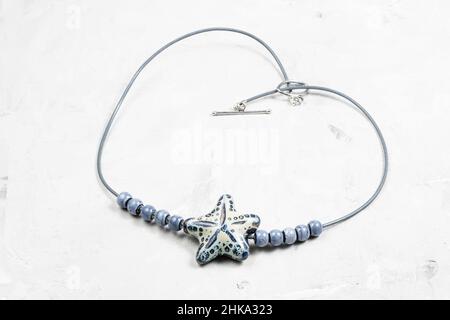 collana artigianale fatta a mano con stelle e perline in ceramica fatte a mano su corda in pelle da vicino su tavola grigia in cemento Foto Stock