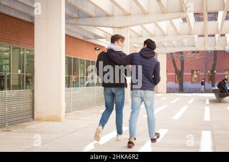 due ragazzi studenteschi dell'università che camminano abbracciandosi l'un l'altro Foto Stock