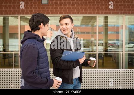 due ragazzi universitari che camminano con una tazza di caffè in mano Foto Stock