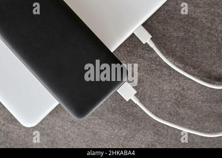 Power Bank ricarica un computer portatile tramite cavo USB di tipo C su sfondo grigio in pietra Foto Stock