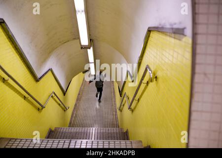 Obiettivo tilt-shift usato - Vista di un giovane che corre irriconoscibile all'interno della stazione metropolitana che passa per diversi treni - piastrelle gialle sulle pareti Foto Stock