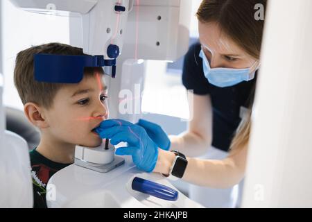 Dentista femminile che prende la radiografia panoramica dei denti ad un bambino usando la moderna macchina a raggi X. Foto Stock