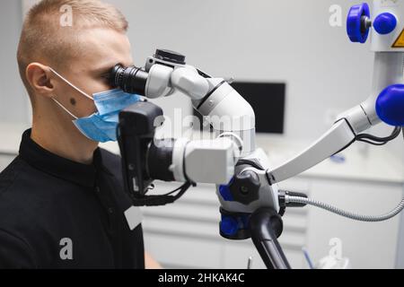 Medico dentista maschile che utilizza il microscopio per il trattamento dentale Foto Stock