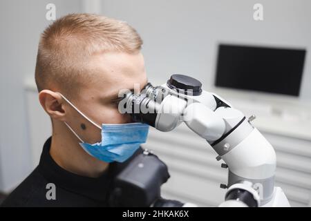 Medico dentista maschile che utilizza il microscopio per il trattamento dentale Foto Stock