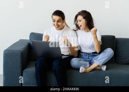 Allegro amorevole giovane coppia di famiglia che celebra il successo di Internet, facendo sì gesto guardando lo schermo del computer, ottenendo in linea lotteria giveaway vincere n Foto Stock