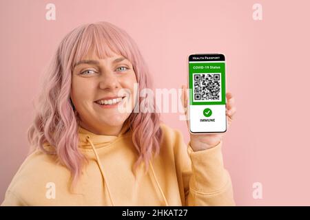 Controllo Covid-19. 30s donna caucasica in maschera con smartphone con pass verde digitale e codice QR sullo schermo. Passaporto sanitario o certificato di Foto Stock