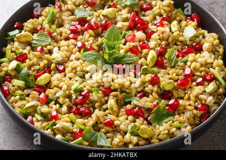 Cibo vegano sano fatto di freekeh con melograno, noci ed erbe primo piano in un piatto sul tavolo. Orizzontale Foto Stock