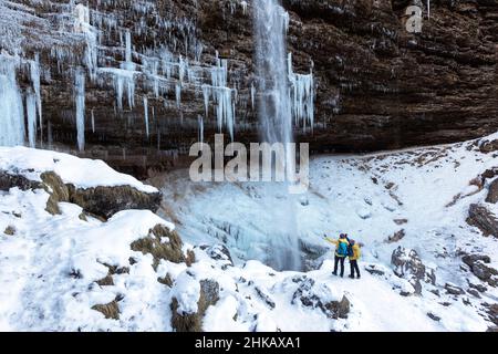 FMother e figlio si trovano di fronte alla cascata ghiacciata della cascata Pericnik in inverno, nel Parco Nazionale del Triglav, Slovenia Foto Stock