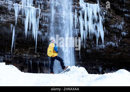 Ragazzo con uno zaino in piedi di fronte alla cascata ghiacciata della cascata di Pericnik in inverno, Parco Nazionale del Triglav, Slovenia Foto Stock