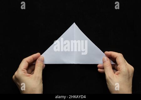 Fare il fiocco di neve. Punto 3. Donna mani che tengono carta aperto triangolo su sfondo nero Foto Stock