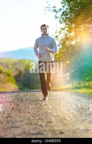 L'uomo che fa jogging nella natura rurale durante la splendida giornata estiva. Sport fitness modello caucasico etnia formazione all'aperto. Foto Stock
