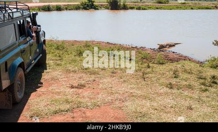 Fotografo che prende le foto di un coccodrillo che prende il sole sulla riva di un foro nella savana del Parco Nazionale di Nairobi vicino a Nairobi, Kenya Foto Stock