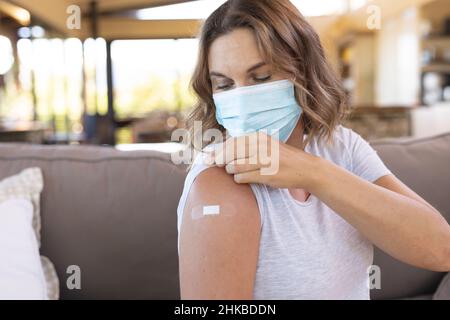 Donna incinta caucasica che indossa una maschera facciale che mostra la spalla dopo aver ricevuto il vaccino Foto Stock