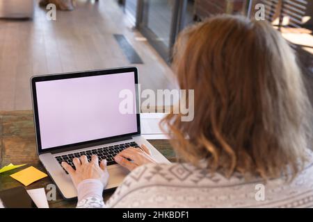 Vista posteriore della donna incinta caucasica che utilizza un computer portatile con spazio per copiare mentre lavora da casa Foto Stock