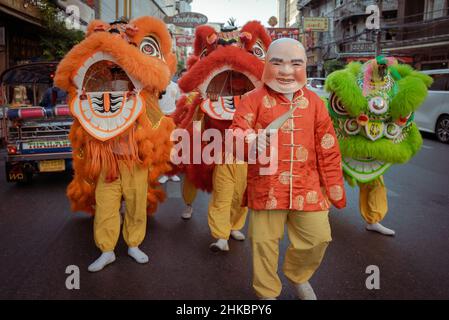 Un uomo in una maschera di Buddha è visto su una strada trafficata con ballerini di leoni dietro di lui.il Capodanno lunare a Bangkok quest'anno è una vicenda più solenne che negli anni precedenti. Il governo aveva tecnicamente cancellato grandi celebrazioni, ma a Chinatown, una troupe di ballerini di leoni rallentò il traffico in arrivo su Yaowrat Road. Su una strada laterale a Wat Lokanukroh, l'unica eccitazione per il giorno è stato lo scoppio di un piccolo fuoco causato quando le grandi candele rosse illuminate crollarono l'una sull'altra; i custodi si precipitarono per un estintore. Molti Thais di discendenza cinese continuarono ad eseguire riti e preghiere al santuario Foto Stock