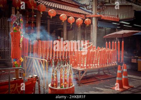 Un custode all'esterno di un tempio illumina un'esposizione di grandi candele rosse. Il Capodanno lunare a Bangkok quest'anno è un affare più solenne che negli anni precedenti. Il governo aveva tecnicamente cancellato grandi celebrazioni, ma a Chinatown, una troupe di ballerini di leoni rallentò il traffico in arrivo su Yaowrat Road. Su una strada laterale a Wat Lokanukroh, l'unica eccitazione per il giorno è stato lo scoppio di un piccolo fuoco causato quando le grandi candele rosse illuminate crollarono l'una sull'altra; i custodi si precipitarono per un estintore. Molti Thais di discendenza cinese continuarono ad eseguire riti e preghiere al santuario undisturbb Foto Stock