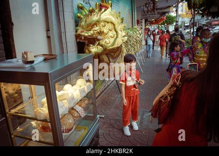 Un bambino pone per una foto accanto ad un burattino di danza dragone in strada.il Capodanno lunare a Bangkok quest'anno è un affare più solenne che negli anni precedenti. Il governo aveva tecnicamente cancellato grandi celebrazioni, ma a Chinatown, una troupe di ballerini di leoni rallentò il traffico in arrivo su Yaowrat Road. Su una strada laterale a Wat Lokanukroh, l'unica eccitazione per il giorno è stato lo scoppio di un piccolo fuoco causato quando le grandi candele rosse illuminate crollarono l'una sull'altra; i custodi si precipitarono per un estintore. Molti Thais di discendenza cinese continuarono ad eseguire riti e preghiere al santuario undist Foto Stock