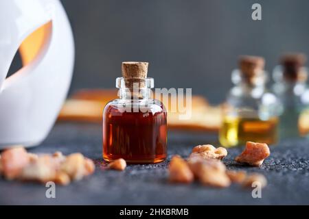 Una bottiglia di olio essenziale styrax con resina di benzoino, con una lampada aromatica sullo sfondo Foto Stock