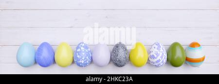 Uovo di Pasqua in fila su legno bianco, testata. Festa di primavera. Vernice color pastello, varie uova di disegno, spazio di copia. 3d rendering Foto Stock