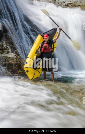 Paddler si erge accanto alla cascata, sollevando la pagaia in aria. Foto Stock