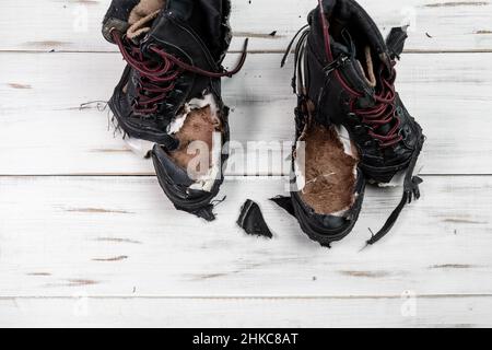 Stivali da scarpe logorati. Sfondo di legno chiaro. Scarpe strappate e rotte. Foto Stock