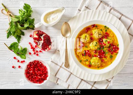 Ash-e Anar, zuppa di melagrana gialla in due pezzi iraniana con polpette di carne, zuppa spessa, in una ciotola bianca su un tavolo di legno bianco testurizzato con ingredienti e Foto Stock