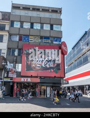 Persone che camminano oltre un grande cartello Coca-Cola a San José, Costa Rica. Foto Stock