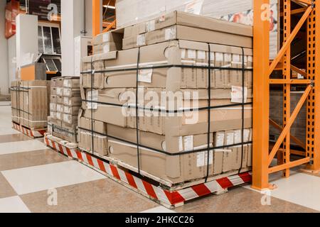 I materiali da costruzione o le merci da costruzione imballate in cartone vengono stoccati su un pallet di legno nel magazzino di un impianto industriale o di un magazzino di ferramenta. Foto Stock