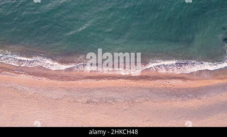 Vista dall'alto delle onde sulla spiaggia. Vacanze estive sul mare. Impronte nella sabbia vicino al mare. Onde dall'alto. Mare e spiaggia. Foto Stock