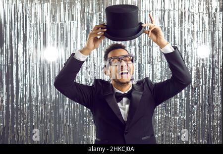 Felice giovane uomo allegro in tuxedo nero e cappello ridendo e divertirsi a festa Foto Stock