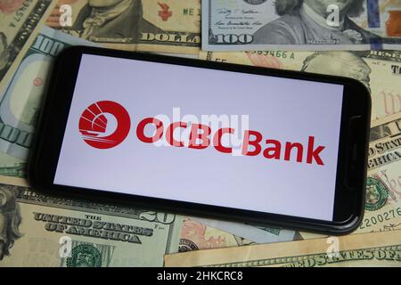 Viersen, Germania - Gennaio 9. 2022: Primo piano del telefono cellulare con il logo di ocbc bancario cinese ocbc, banconote in dollari USA sfondo Foto Stock