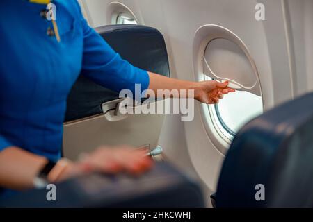 Donna assistente di volo che chiude la finestra in aereo Foto Stock