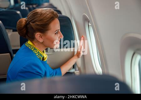 Donna gioiosa stewardess guardando fuori la finestra in aereo Foto Stock