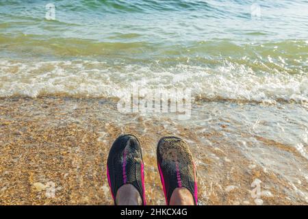Vista delle scarpe da nuoto sui piedi di un uomo sullo sfondo del mare. Grecia. Foto Stock