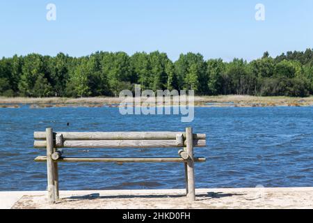 Panchina di fronte al fiume con una foresta sullo sfondo Foto Stock