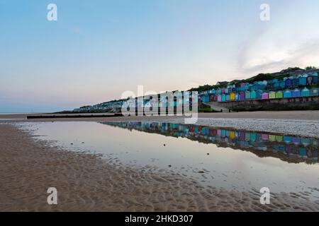 Colorate capanne sulla spiaggia costeggiano il lungomare di Walton-on-the-Naze, North Essex Coastline, Regno Unito. Riflessi creati in piscine lasciate dietro a bassa marea. Foto Stock