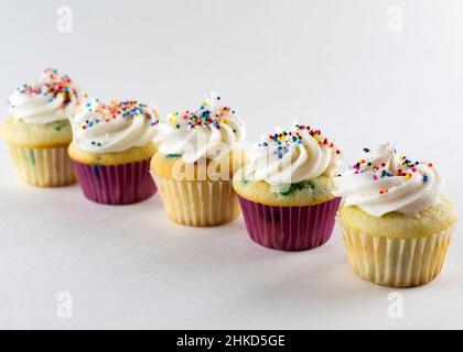 Cinque mini cupcake primavera con pick e liner bianchi disposti in una fila diagonale. Concentratevi sul cupcake anteriore con altri cupcake che si sfocano in bac Foto Stock