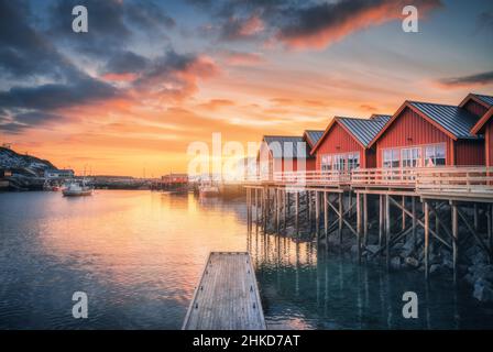 Rorbu rosso su pali di legno sulla costa del mare, piccolo molo, cielo arancione Foto Stock
