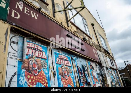 Negozio chiuso. Salito in su l'ex deposito della seconda mano con i manifesti di pubblicità strappati e strappati del circo. Edificio in decadimento con etichette adesive. Immagine clown Foto Stock