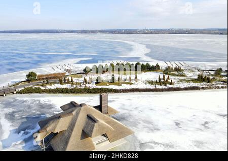 Inverno bellissimo paesaggio con un fiume ghiacciato e piccole case con tetti di canna sull'isola. Stile rustico, tetto di paglia, gabbia. Foto aerea drone vi Foto Stock